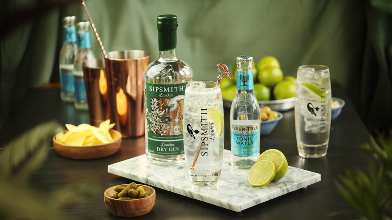 Tonic cocktail glass with slice of lime, bottle of Sipsmith London gin and mediterranean fever tree tonic in the background.