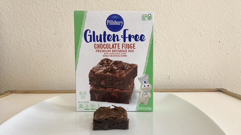 Pillsbury Gluten Free Chocolate Fudge Premium Brownie Mix box alonside a baked brownie
