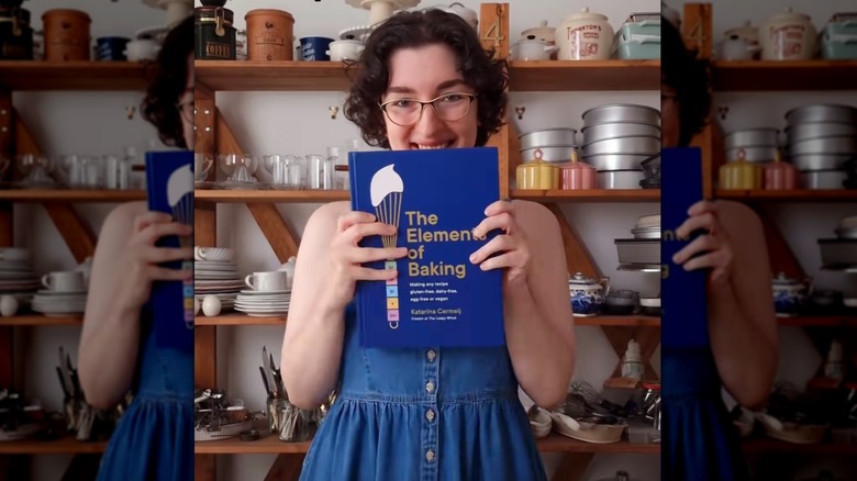 The Loopy Whisk holding up book called The Elements of Baking