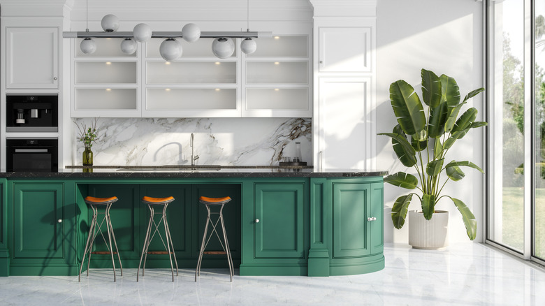 Modern white kitchen with large plant and green island, three stools