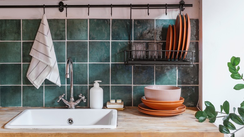 Green blue kitchen backsplash tile behind white sink, dishes