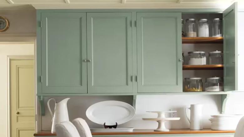 light farmhouse kitchen with soft green cabinets filled with pantry jars, dark table