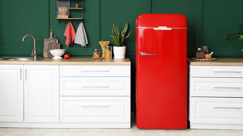 Dark green kitchen all with bright red refrigerator, sink, cabinets