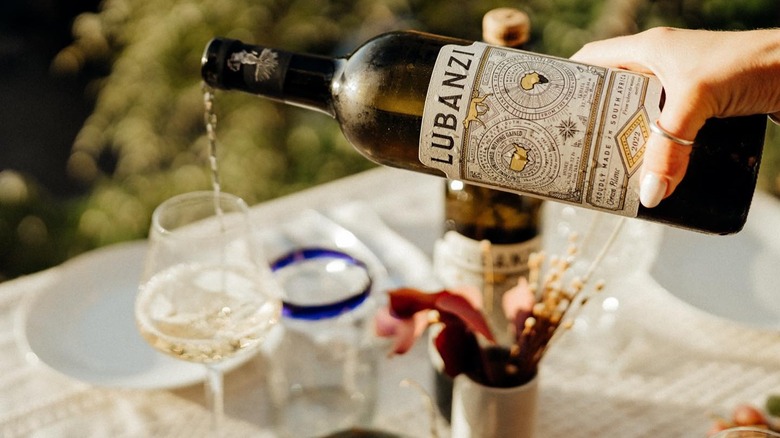 hand pouring white wine into glass