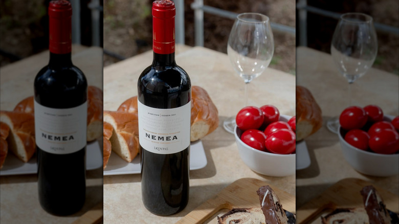 bottle of red wine on a dinner table with bread and tomatoes in the back