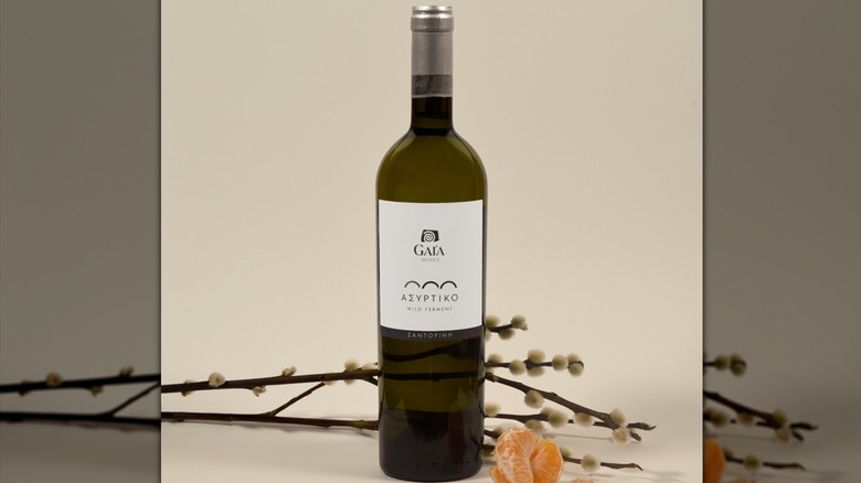 bottle of assyrtiko greek wine against a beige background next to twigs and tangerines