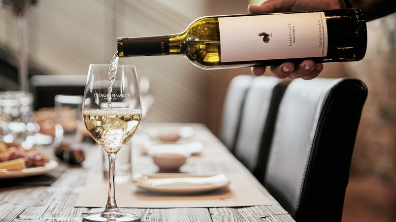 person pouring white Savatiano wine glass from bottle in a restaurant setting