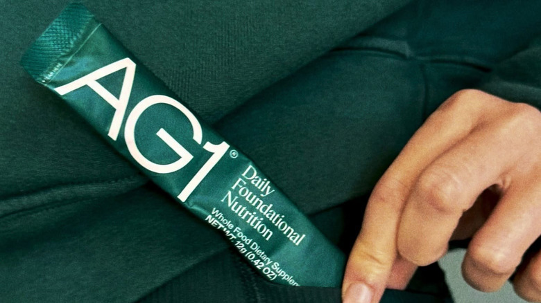 A woman pulling out a satchet of AG1 from the pocket of her yoga pants, dressed in the brand colors