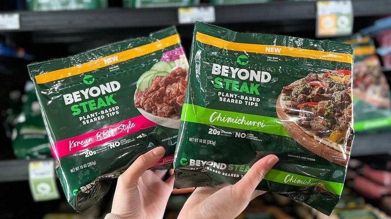 A woman holding two packages of Beyond Steak held up against an entire grocery store aisle of Beyond Meat.