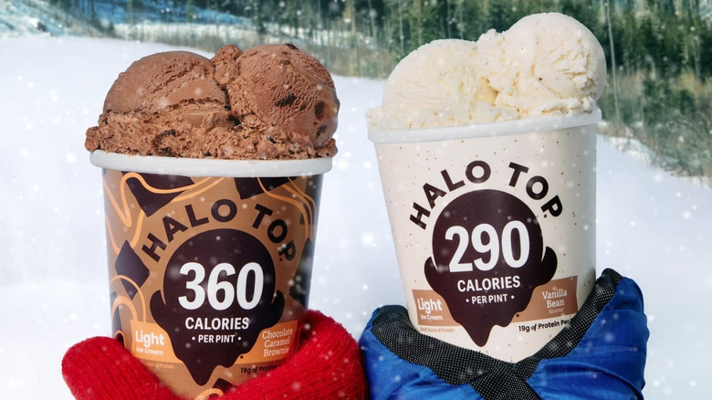 Two gloved hands holding two pints of halo top in Vanilla Bean and Chocolate Caramel Brownie flavors against the backdrop of snow and snow capped mountains.