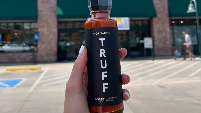 A woman's hand holding a bottle of Truff Hot Sauce in front of a Whole Foods.