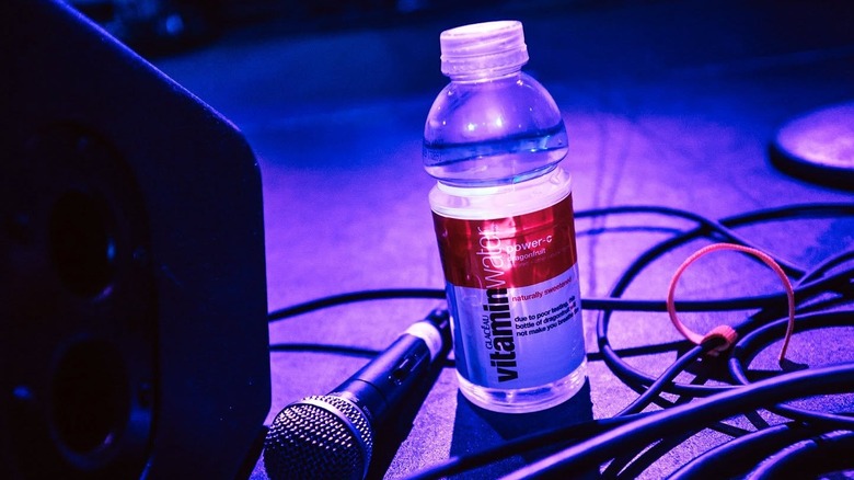 A bottle of Vitaminwater placed on a stage next to a mic and surrounded by several wires.