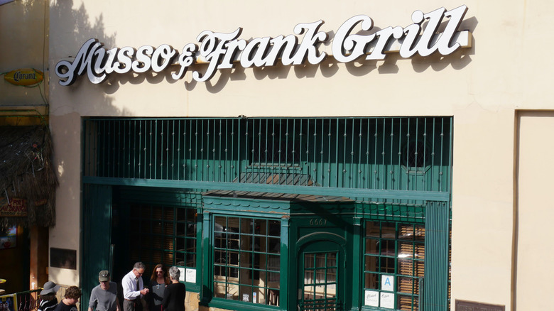 Customers wait outside the green iron gates of the Musso & Frank Grill