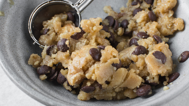 A bowl of chocolate chip cookie dough with a metal scooper