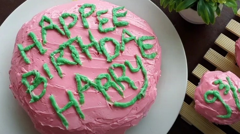 Messy pink and green frosted cake decorated with the words "Happee Birthdae Harry".