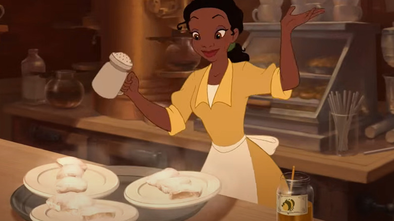 tiana dusting beignets with powdered sugar