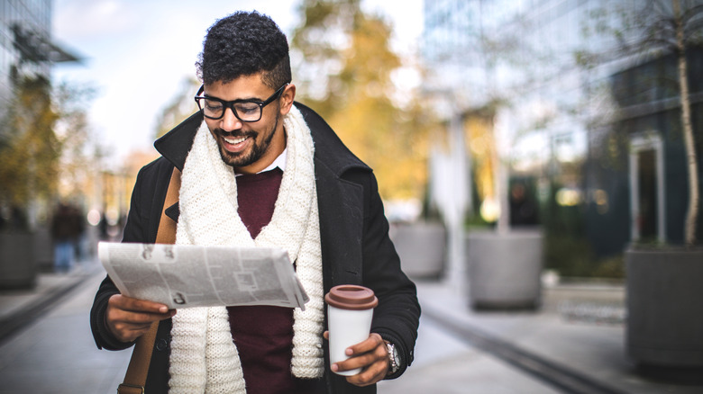 Man drinking coffee on street while holding newspaper