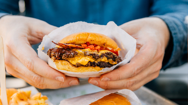 Person holding cheeseburger wrapped in paper