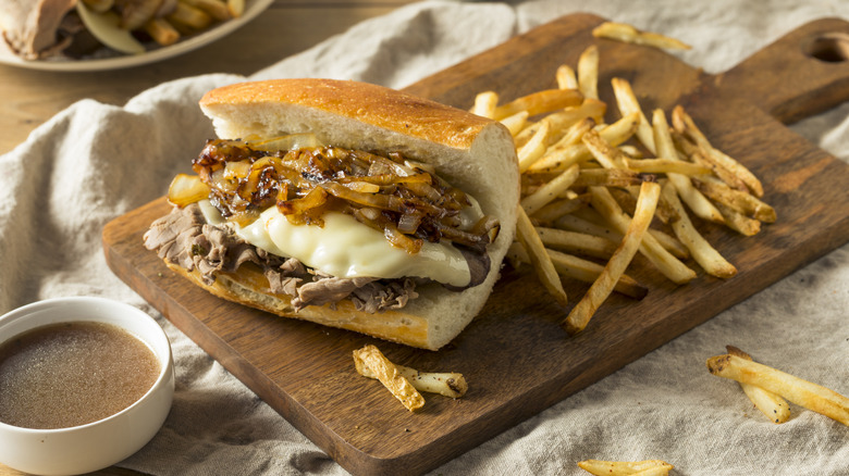 French dip sandwich on a wooden platter, next to fries and au jus