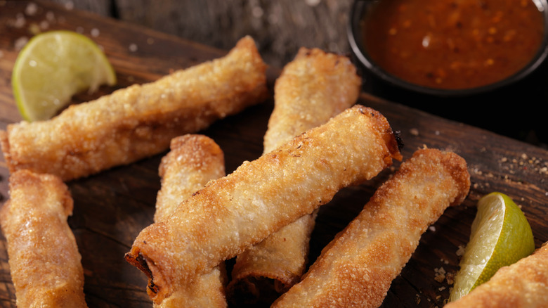 Taquitos on a wooden plate with limes and salsa
