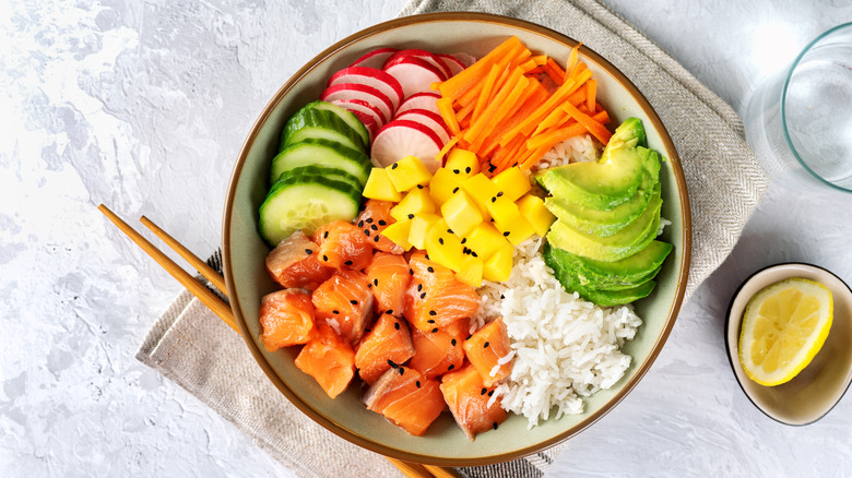 Salmon poke bowl with sliced avocado, mango, cucumber, radish, and carrot