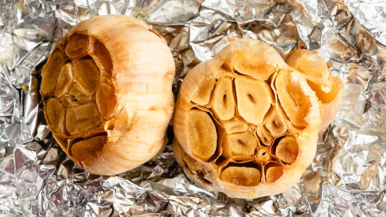 Roasted garlic bulbs drizzled with extra virgin olive oil and sea salt on tin foil