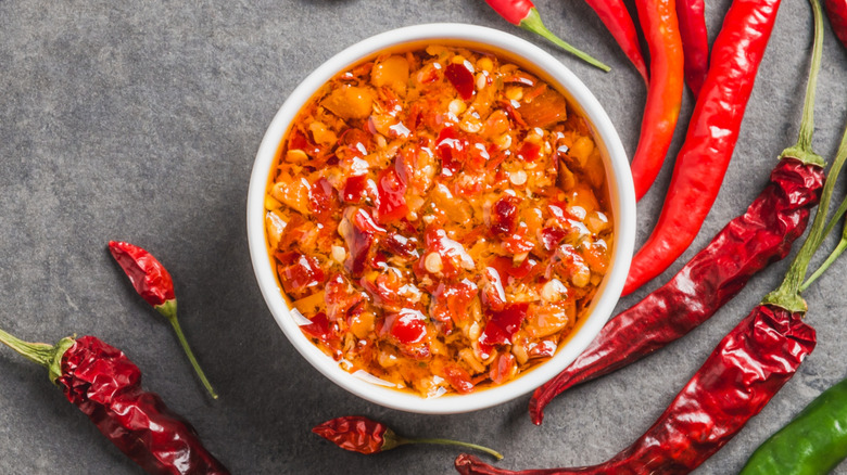 chili paste in white dish surrounded by chiles on dark grey surface