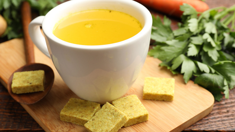 bouillon cubes, broth, parsley and vegetables on wooden table with white cup of broth