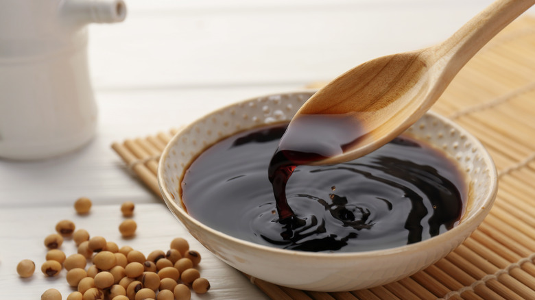 soy sauce in bowl with spoon next to soybeans on white wooden table