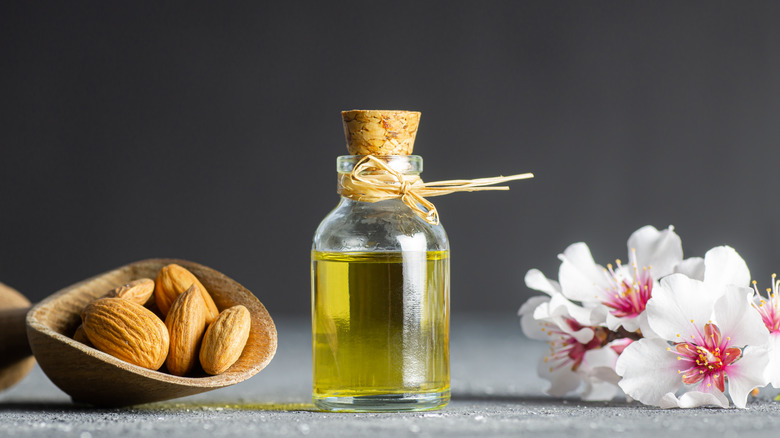 Glass bottle of Almond oil and almond nuts , almonds with almond tree flowers on table. Almond background concept with copy space.
