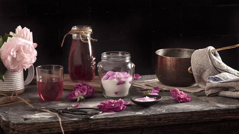 preparation of rose petals syrup in copper pan and glass bottle on rustic table,