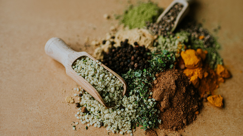 Pile of various coloured and textured herbs, spices and seasonings on a wooden table with two wooden scoops. Space for copy.