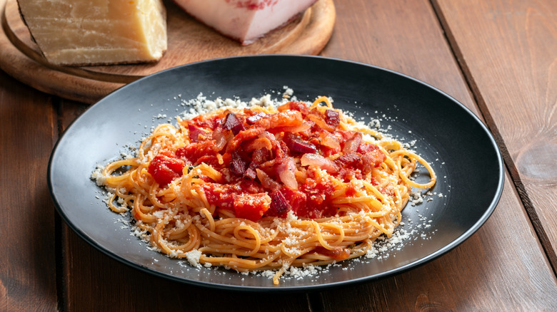 A plate of pasta Amatriciana with pecorino and guanciale in the background