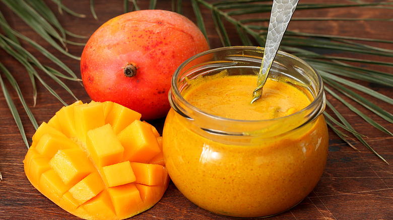 Amba sauce in an open jar with a spoon beside fresh mangos