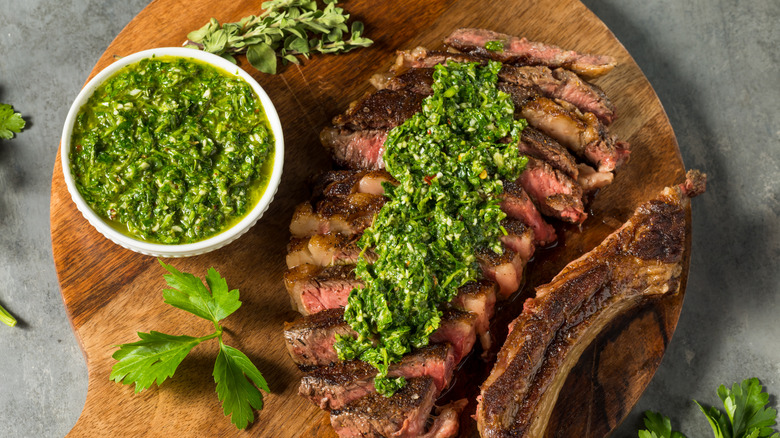 Chimichurri in a bowl and topping sliced steak on a cutting board