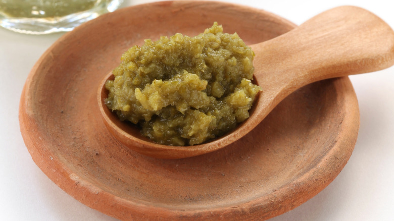 Yuzu kosho paste on a wooden spoon sitting in a pottery saucer