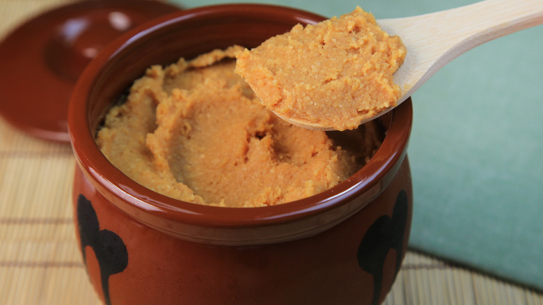 Spooning miso paste out of a small brown crock