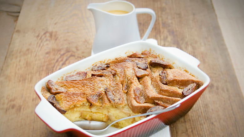 Bread and butter pudding in baking dish with pitcher of custard in background