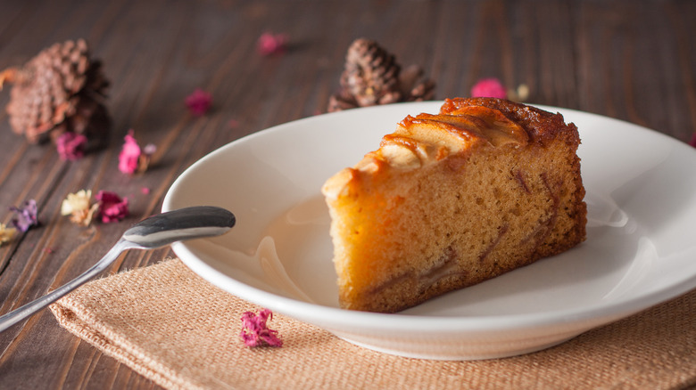 Slice of Irish apple cake on plate with spoon, dried flowers and pinecones scattered in background