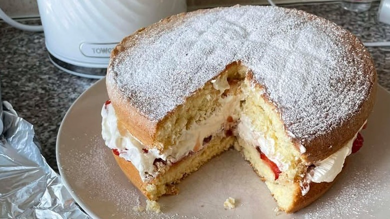 Two-tiered, sugar-dusted sponge cake filled with strawberries and cream on plate