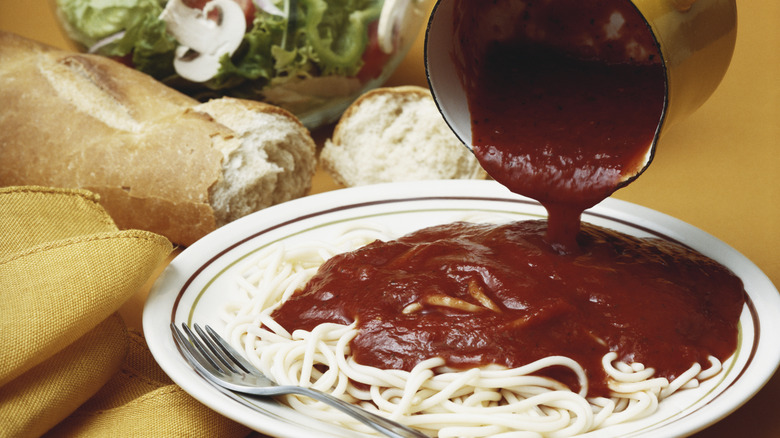 Tomato sauce being poured on spaghetti