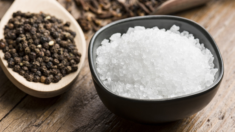 a bowl of sea salt crystals and a spoonfullof black peppercorns