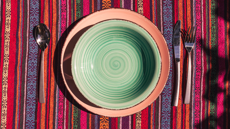 Overhead view image of a plate and soup bowl with cutlery on a colorful striped tablecloth