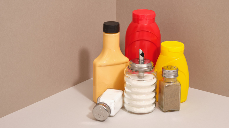 Bottles of ketchup, mustard, salt, and pepper against a beige backdrop