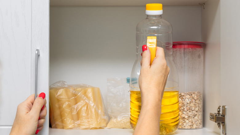 Hand removing a bottle of sunflower oil from a kitchen cabinet