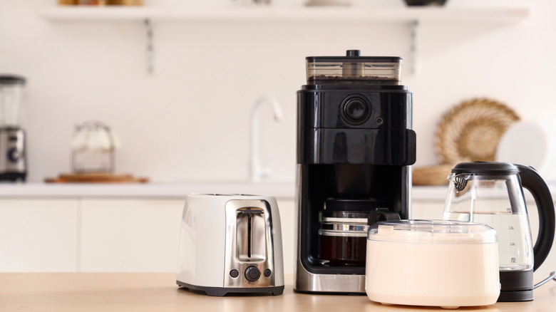 Wooden table with a set of kitchen appliances, including a toaster, electric kettle, and coffee maker