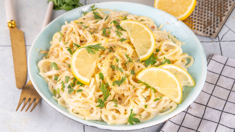Bowl of creamy lemon pasta garnished with fresh parsley and lemon wedges