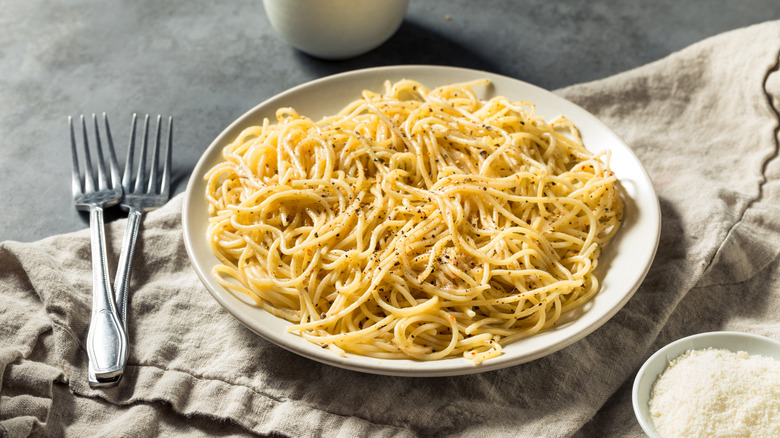 Plate of cacio e pepe pasta next to bowl of grated Parmesan