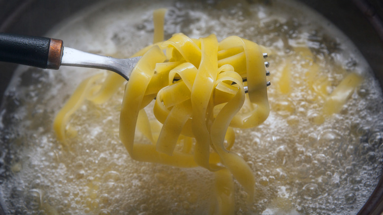 Lifting forkful of tagliatelle pasta from pot of cooking water