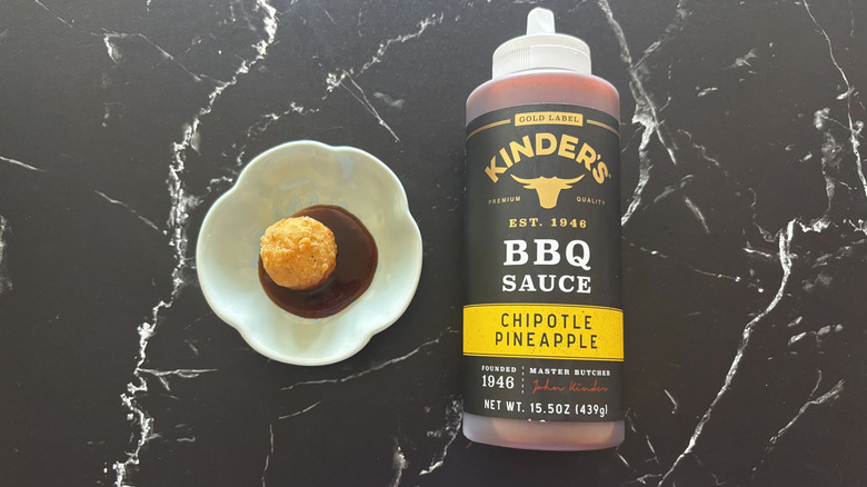 Kinder's chipotle pineapple BBQ sauce bottle next to chicken nugget and sauce on plate